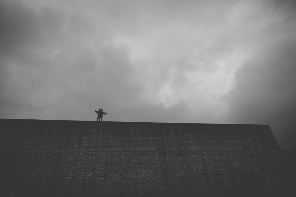 le photographe fait monter le couple en haut du mur sous un ciel orageux