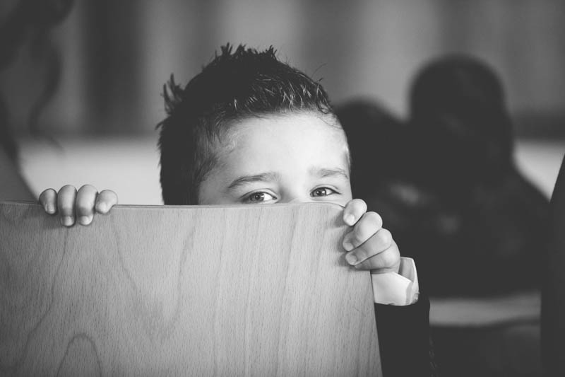 young boy hidding behind chair