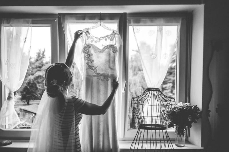 la mariée suspend sa robe à la fenetre de sa chambre