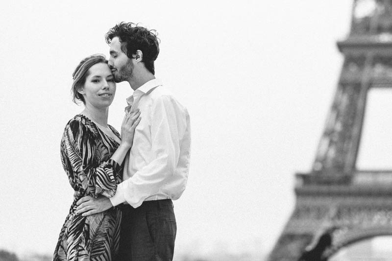 un jeune homme embrasse tendrement sa femme devant la tour Eiffel